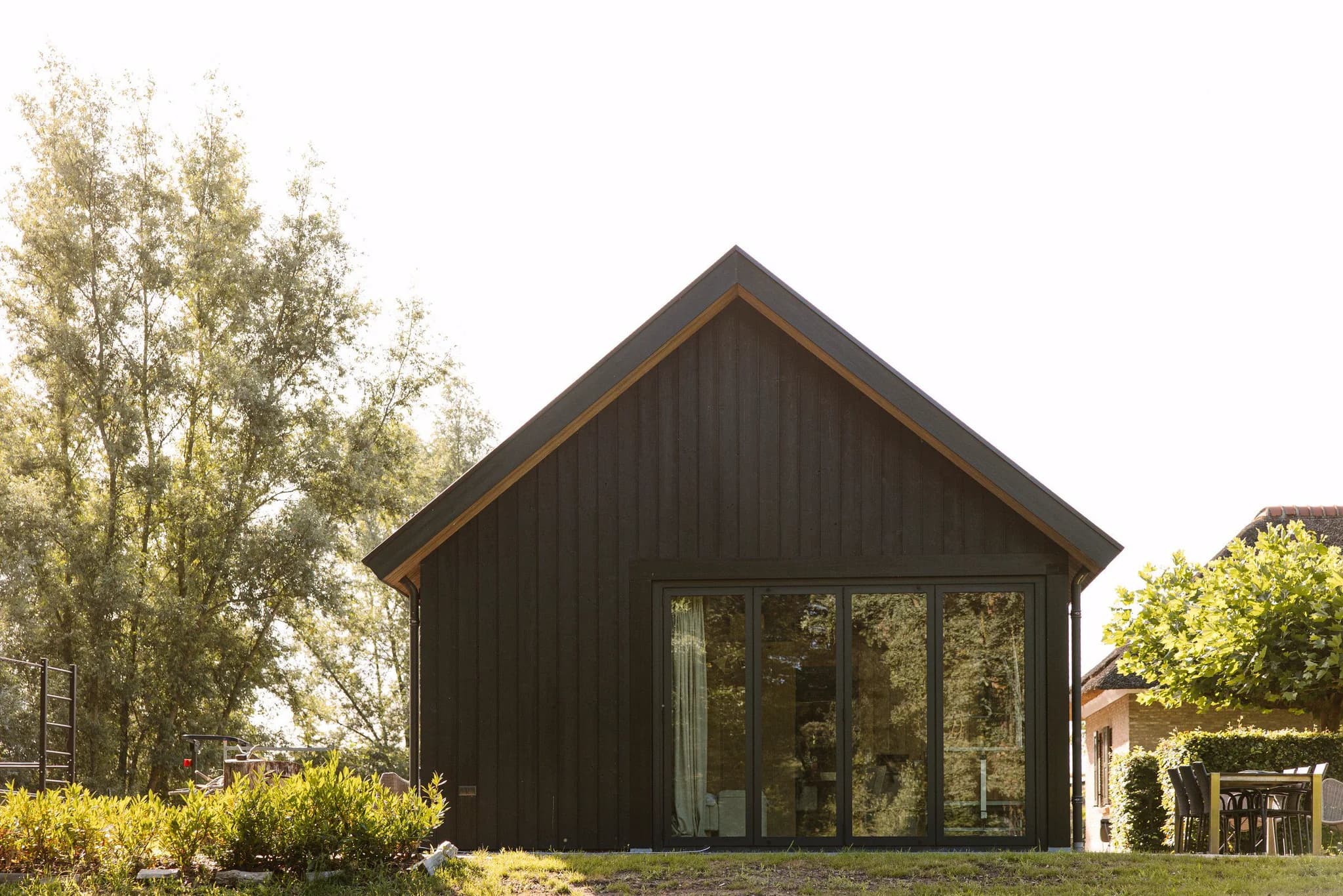 Achterkant van een zwart houten huis met grote glazen schuifdeuren en groen rondom.