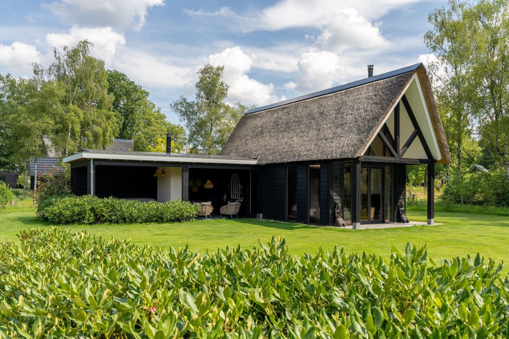 Zwart houten huis met rieten dak en groene tuin bij zonnig weer