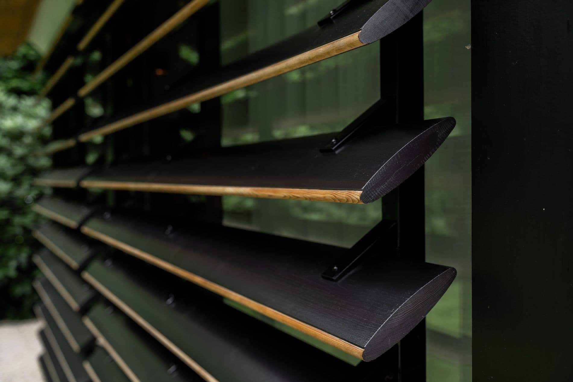 Close-up van schuine zwarte houten lamellen met zichtbare houten randen en metalen bevestiging
