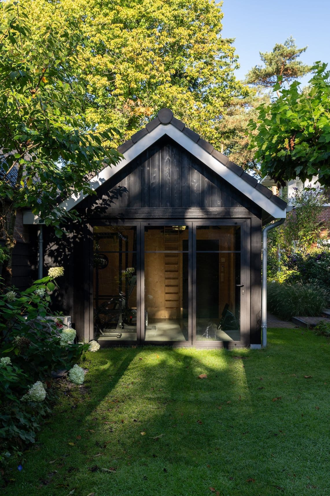 Zwart tuinhuis met glazen deuren en zadeldak in groene tuin