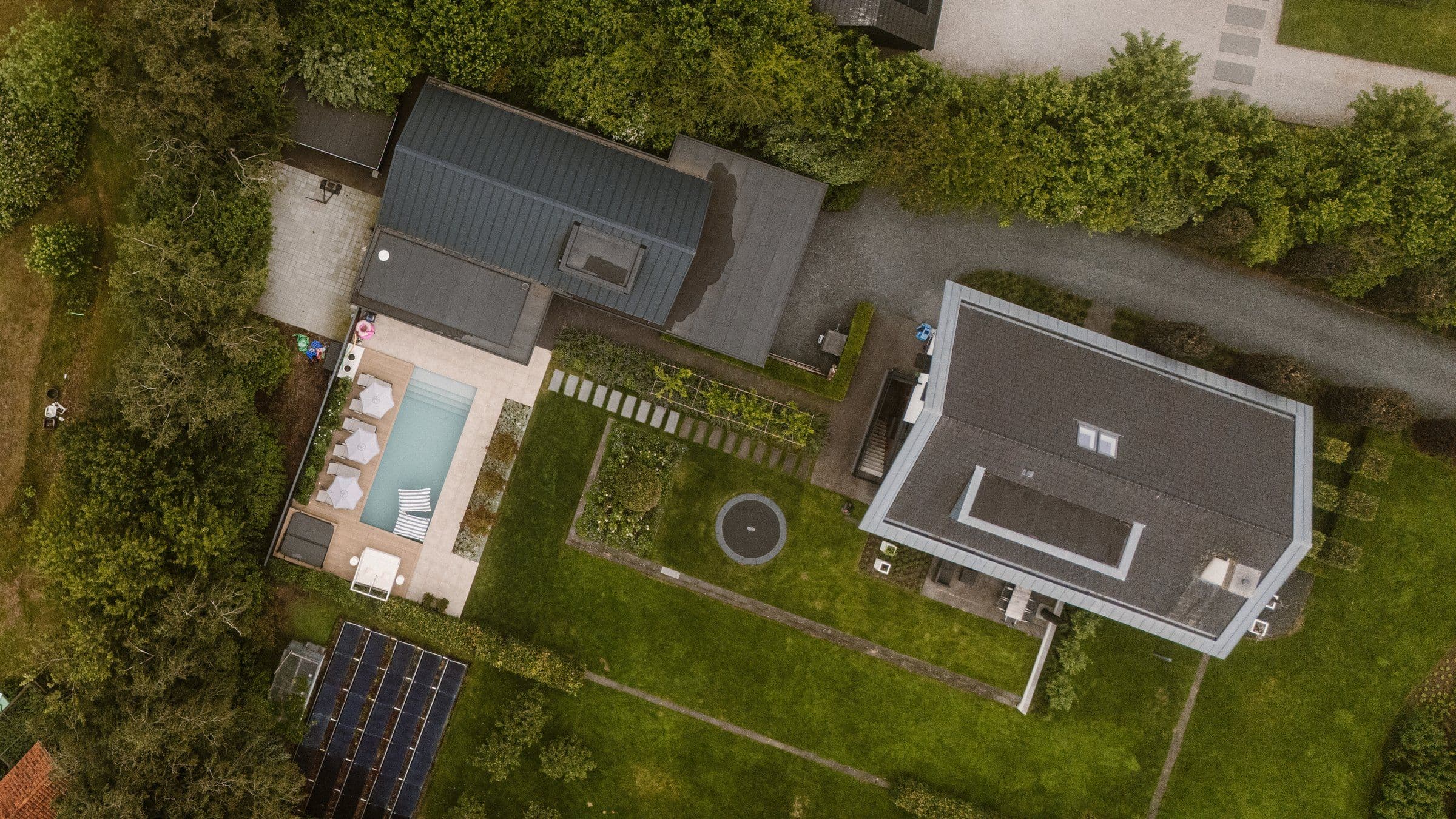Luchtfoto van een woning met een zwembad, terras en groene tuin met trampoline
