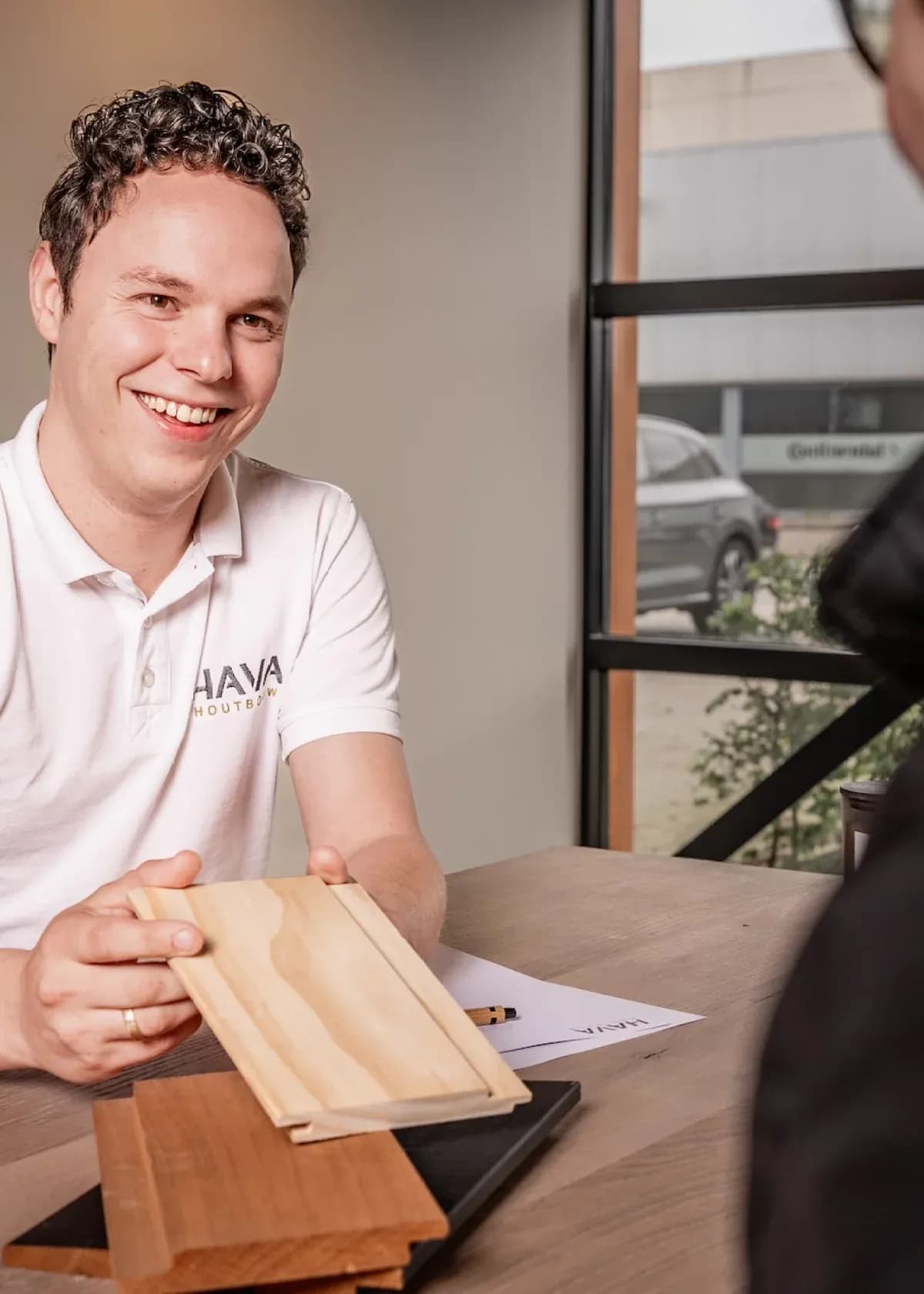 Man in witte polo laat houten vloerdelen zien aan een persoon aan tafel