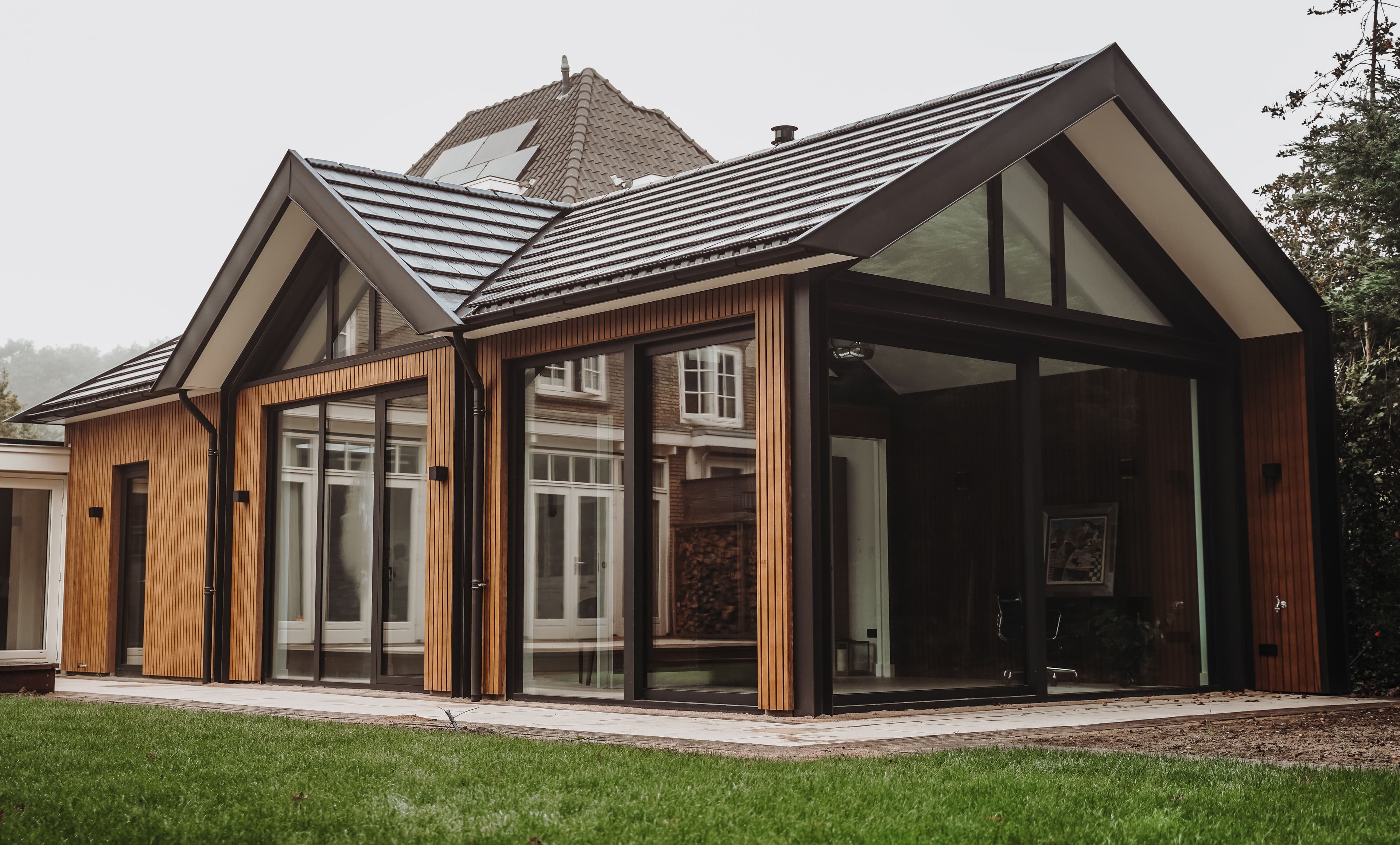 Moderne aanbouw met grote ramen en houten gevelbekleding naast grasveld