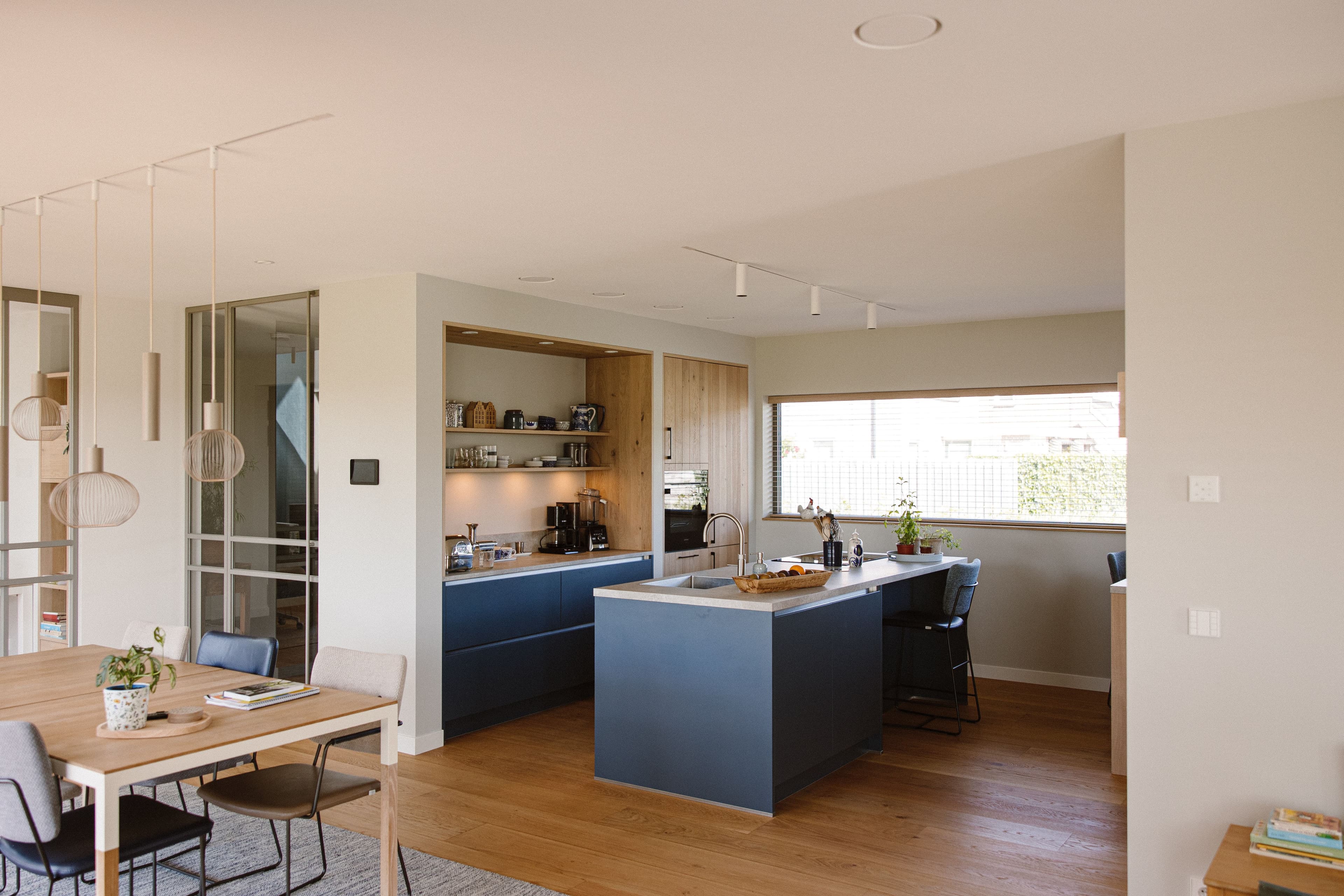 Moderne keuken met een kookeiland in het midden, blauwe kasten en een houten eettafel met stoelen.