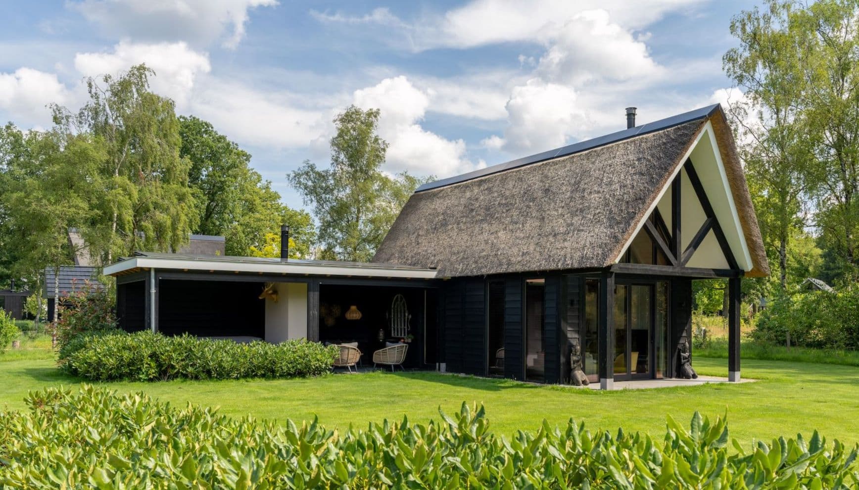Zwarte vakantiewoning met rieten dak en grote ramen in groene tuin
