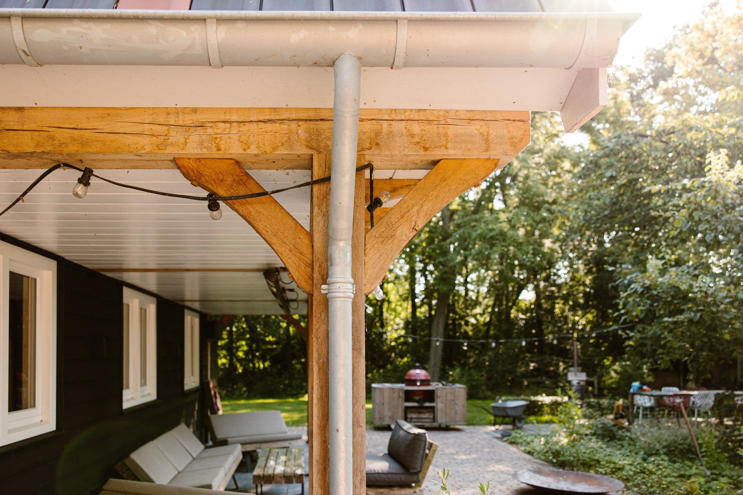 Terrasoverkapping van hout met zitbanken en een buitenkeuken in een groene tuin bij zonlicht