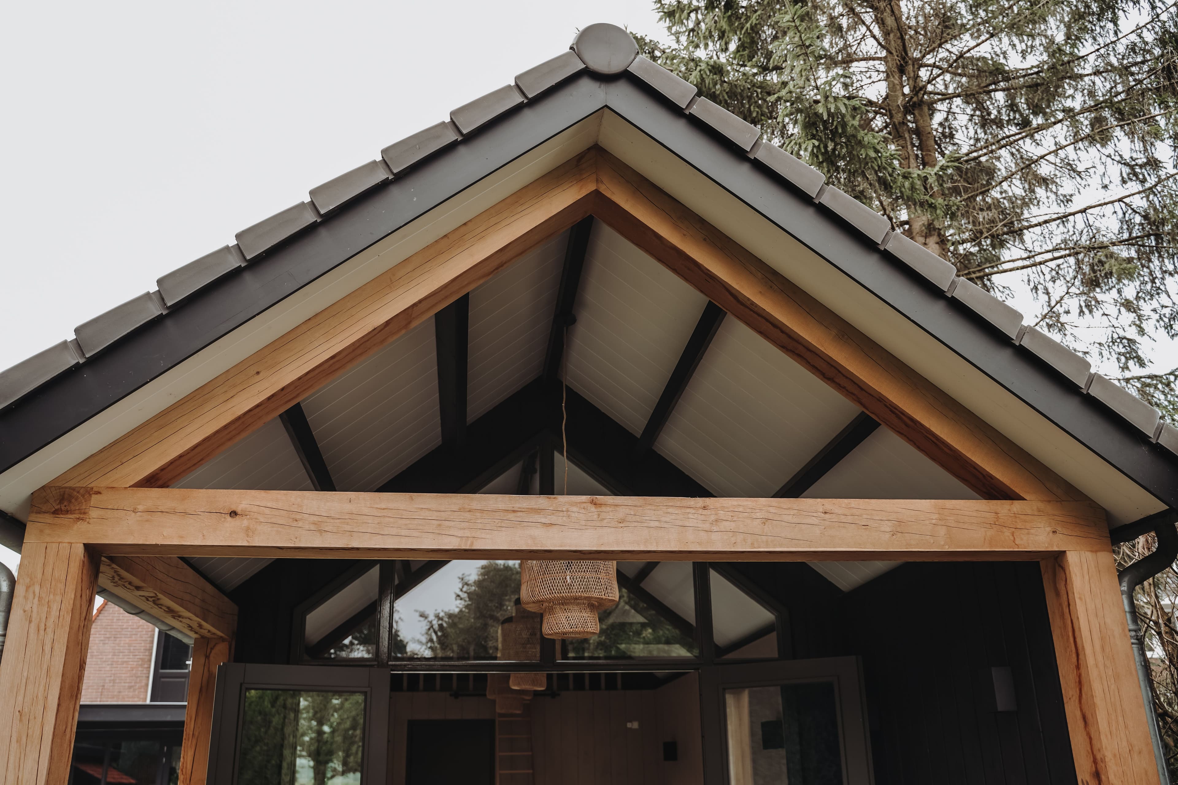 Voorgevel van een modern houten huis met een zadeldak en een houten overkapping met glas