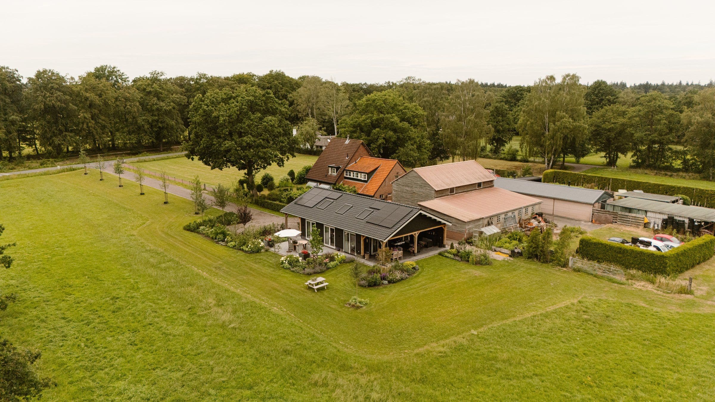 Woonboerderij met grote groene tuin en schuren in een landelijke omgeving gezien vanuit de lucht